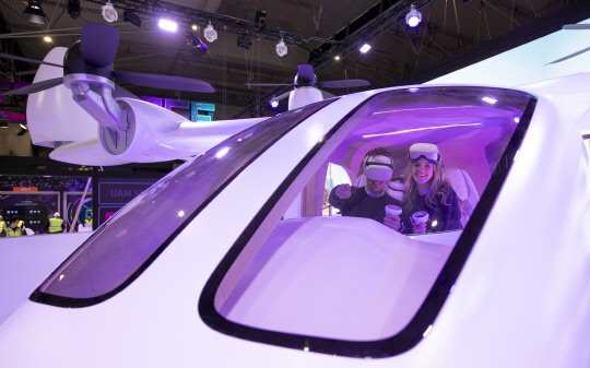 스페인 바르셀로나 'MWC 2023' 전시관에서 현지 모델들이 UAM 모형에 탑승해 2030년의 서울을 배경으로 비행하는 서비스를 체험하고 있다. SKT 제공